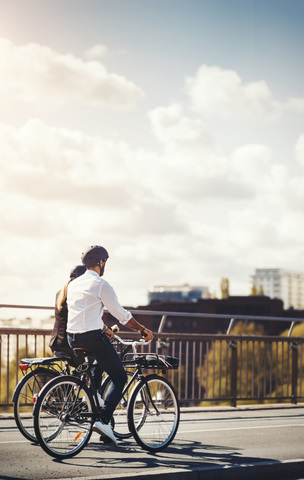 Rückansicht von Geschäftsleuten auf Fahrrädern auf einer Brücke gegen den Himmel, lizenzfreies Stockfoto