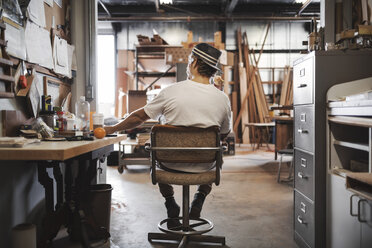 Rückansicht eines Tischlers auf einem Stuhl in der Werkstatt - MASF04051