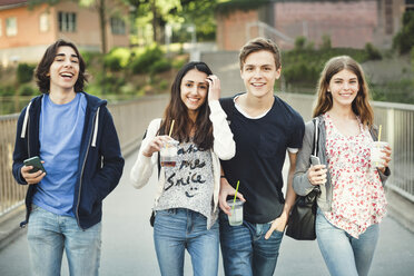 Portrait of happy teenagers holding disposable glasses and smart phones on bridge - MASF04075