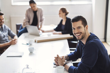 Portrait of happy young businessman with colleagues in background at conference room - MASF04079