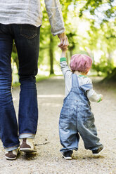 Rear view of baby girl holding mother's hand while walking on dirt road - MASF04090