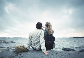 Rear view of couple taking selfie while sitting on rock by sea - MASF04095