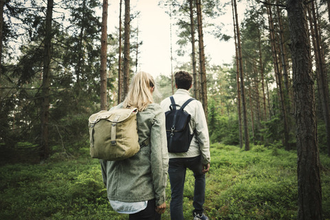 Rear view of couple carrying backpacks while walking through forest stock photo