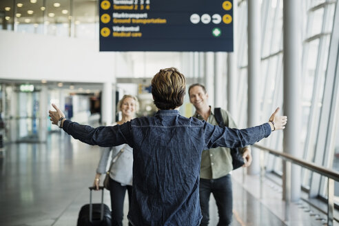 Rückansicht eines Geschäftsmannes, der mit ausgestreckten Armen steht und seine Kollegen am Flughafen begrüßt - MASF04098