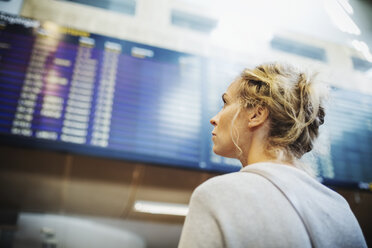 Rückansicht einer Geschäftsfrau mit Blick auf die Ankunft-Abflug-Tafel im Flughafen - MASF04100