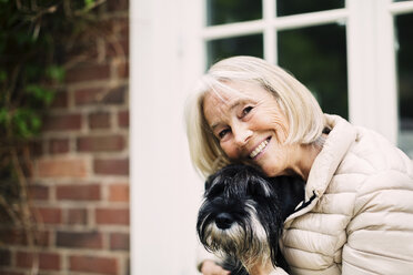 Porträt einer glücklichen älteren Frau mit Hund vor dem Haus - MASF04102