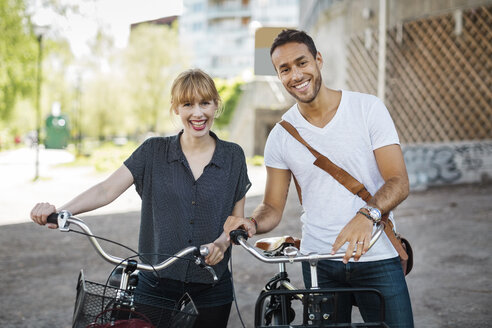 Porträt von glücklichen Geschäftsleuten mit Fahrrädern, die auf einer Stadtstraße stehen - MASF04115