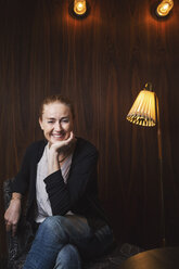 Porträt einer glücklichen Geschäftsfrau, die auf einem Stuhl in einer Bürohalle sitzt - MASF04126