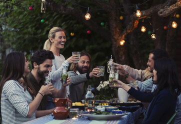 Multi-ethnic friends toasting drinks at dinner table in yard - MASF04136