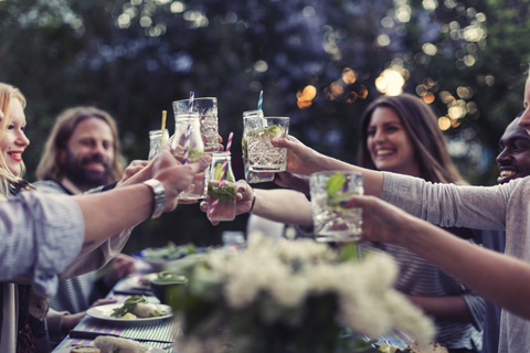 Multi-ethnic friends toasting mojito glasses at dinner table in yard stock photo