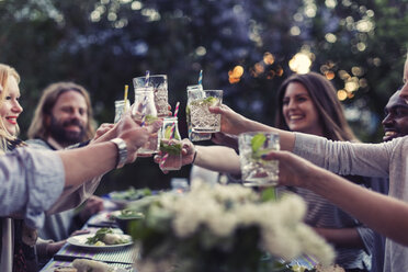 Multi-ethnic friends toasting mojito glasses at dinner table in yard - MASF04138