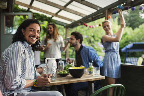 Porträt eines glücklichen Mannes, der am Tisch sitzt und eine Party mit Freunden im Sommerhaus genießt, lizenzfreies Stockfoto