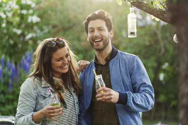 Portrait of happy man enjoying with woman while holding drink bottles at summer party - MASF04143