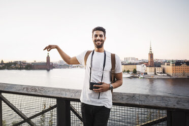 Optische Täuschung eines glücklichen männlichen Touristen, der ein Gebäude in der Stadt gegen den klaren Himmel hält - MASF04146