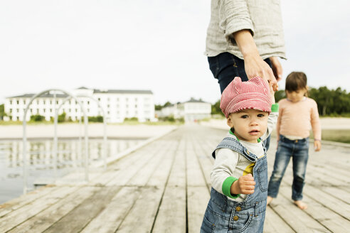 Porträt eines kleinen Mädchens, das mit seiner Familie auf einem Pier am Strand steht, gegen einen klaren Himmel - MASF04149