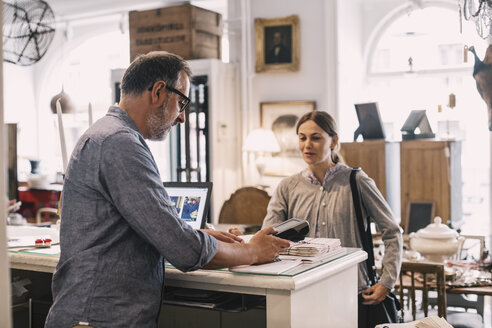 Owner using card reader in front of female customer at shop counter - MASF04155