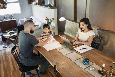 Mother working on laptop while father assisting son in doing homework at dining table - MASF04170