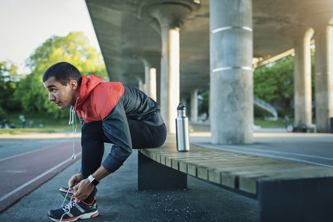 Man tying shoelace while sitting on bench stock photo