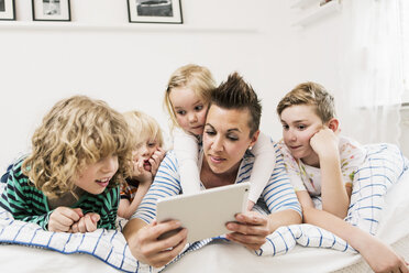 Mother and children using digital tablet lying in bed at home - MASF04177