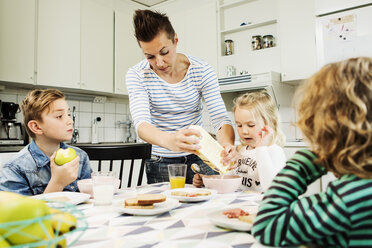 Mother serving breakfast to children at dining table in kitchen - MASF04178