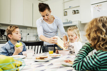 Mutter serviert den Kindern am Esstisch in der Küche das Frühstück - MASF04178