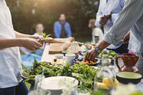 Midsection of friends preparing food at dining table in backyard - MASF04187