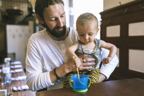 Mid erwachsenen Vater mit Sohn rühren Löffel in Tasse im Restaurant Tabelle, lizenzfreies Stockfoto