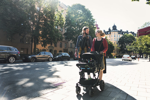 Mid erwachsenen Eltern mit Baby Junge und Kinderwagen zu Fuß auf dem Bürgersteig in der Stadt, lizenzfreies Stockfoto