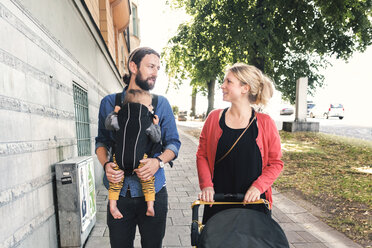 Mid adult parents with baby boy and stroller walking on sidewalk - MASF04196