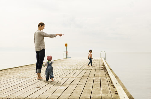 Mutter, die ihrem kleinen Mädchen etwas zeigt, während sie auf einem Pier am Meer steht, gegen den Himmel - MASF04201