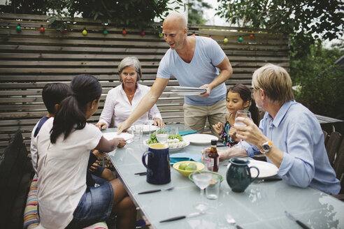 Mann serviert der Familie am Esstisch im Freien das Essen - MASF04204