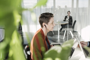 Reife Geschäftsfrau trägt Kopfhörer beim Sitzen im Büro - MASF04207