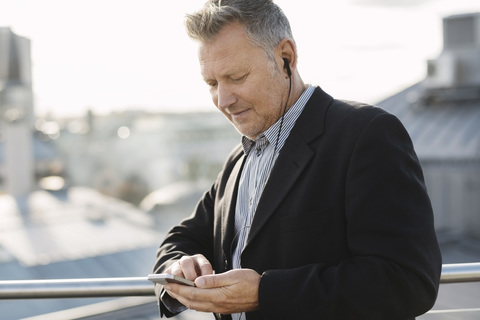 Älterer Geschäftsmann hört Musik über das Telefon, während er im Büro steht, lizenzfreies Stockfoto