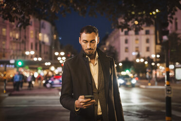 Mann benutzt Smartphone auf einer nächtlichen Straße in der Stadt - MASF04213