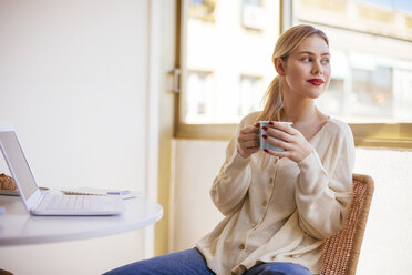 Blonde woman with cup of coffee looking out of the window - EBSF02390