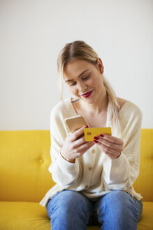 Blonde woman using smartphone and using bank card at home - EBSF02397