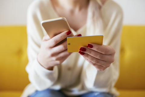 Blonde Frau mit Smartphone und Bankkarte zu Hause, lizenzfreies Stockfoto