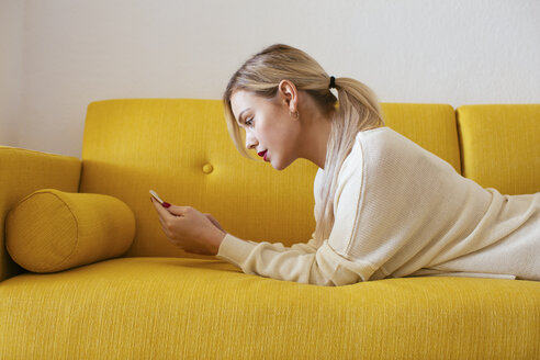 Blonde Frau liegt auf dem Sofa und benutzt ihr Smartphone zu Hause - EBSF02401