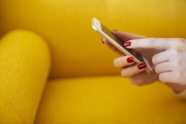 Woman using smartphone, yellow sofa - EBSF02404