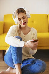 Blonde woman with headphones using smartphone at home - EBSF02410