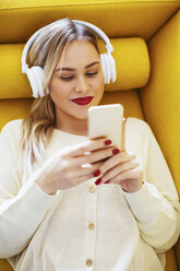 Blonde woman with headphones using smartphone at home - EBSF02411