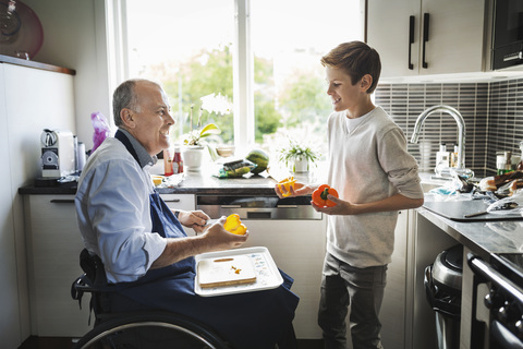 Glücklicher behinderter Vater im Rollstuhl bereitet mit seinem Sohn in der Küche Essen zu, lizenzfreies Stockfoto