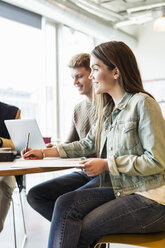 Happy woman writing while sitting with friend in university classroom - MASF04231