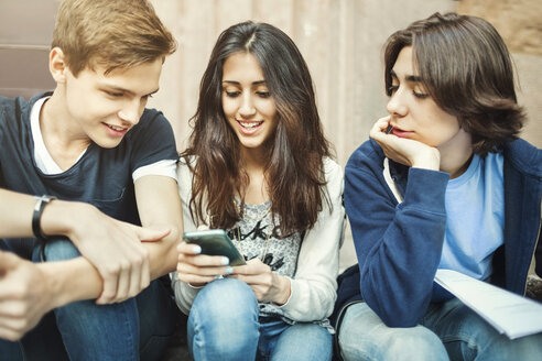 Glückliches Mädchen, das ein Smartphone benutzt, während es mit männlichen Freunden auf einer Treppe sitzt - MASF04239
