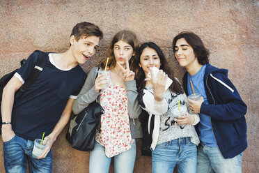 Happy teenagers gesturing while taking selfie against wall - MASF04240