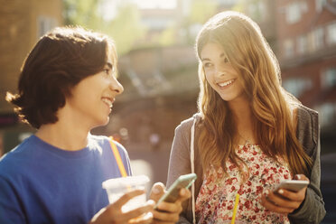 Happy teenagers looking at each other while holding smart phones outdoors - MASF04241