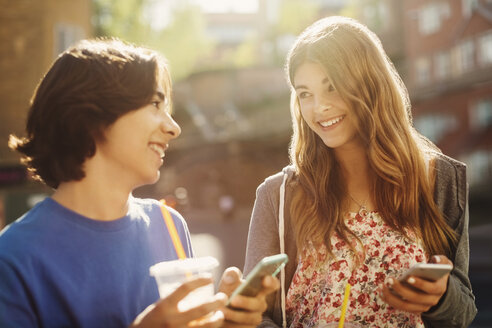 Glückliche Teenager, die sich gegenseitig ansehen, während sie ihre Smartphones im Freien halten - MASF04241