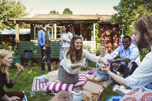 Glückliche Frau serviert Freunden im Hinterhof während einer Sommerparty Pizza - MASF04246