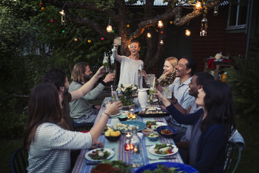 Glückliche Frau stößt mit Freunden am Esstisch auf ein Getränk an, während sie eine Dinnerparty im Freien genießt - MASF04247