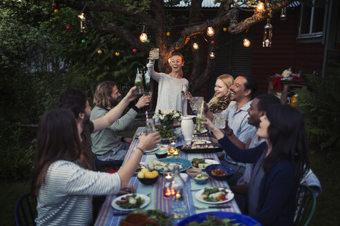 Happy woman toasting drink to friends at dining table while enjoying outdoor dinner party - MASF04247